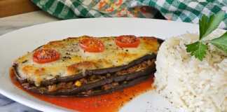 Ψητές Μελιτζάνες με κιμά και τυρί Ένα πιατο με ψητές μελιτζάνες γεμισμένες με κιμά και καλυμμένες με λιωμένη μοτσαρέλα και ντοματίνια, έτοιμες για σερβίρισμα.