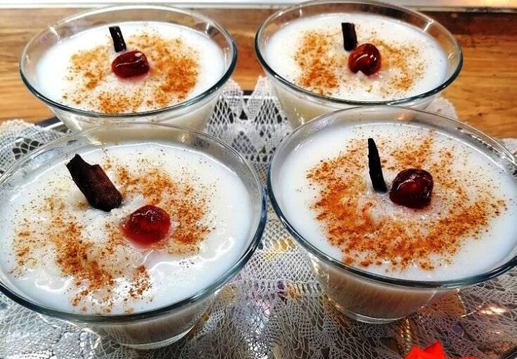 Μπολάκια με ζεστό, κρεμώδες ρυζόγαλο πασπαλισμένο με κανέλα, τοποθετημένα σε ξύλινη επιφάνεια.