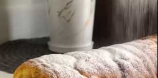 Μια φέτα ρολό μήλου που δείχνει το τυλιγμένο παντεσπάνι και τη γέμιση μήλου στο εσωτερικό, πασπαλισμένο με άχνη ζάχαρη.