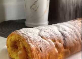 Μια φέτα ρολό μήλου που δείχνει το τυλιγμένο παντεσπάνι και τη γέμιση μήλου στο εσωτερικό, πασπαλισμένο με άχνη ζάχαρη.