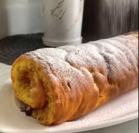 Μια φέτα ρολό μήλου που δείχνει το τυλιγμένο παντεσπάνι και τη γέμιση μήλου στο εσωτερικό, πασπαλισμένο με άχνη ζάχαρη.