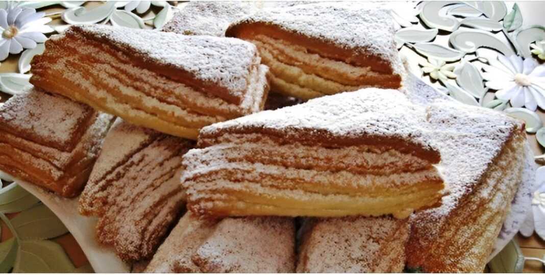 Πιάτο με χρυσαφένιες, τραγανές σφολιάτες κομμένες σε τρίγωνα, πασπαλισμένες με ζάχαρη άχνη, έτοιμες για σερβίρισμα.