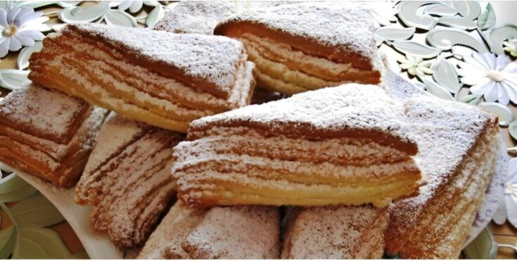 Πιάτο με χρυσαφένιες, τραγανές σφολιάτες κομμένες σε τρίγωνα, πασπαλισμένες με ζάχαρη άχνη, έτοιμες για σερβίρισμα.