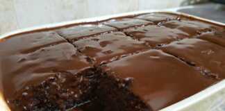 Ένα ολόκληρο, τετράγωνο σοκολατένιο κέικ με γυαλιστερό γλάσο σοκολάτας στην κορυφή, τοποθετημένο πάνω σε μια σχάρα για να κρυώσει.