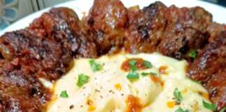 Ένα πιάτο με μακρόστενα σουτζουκάκια βουτηγμένα σε κόκκινη σάλτσα ντομάτας, δίπλα σε μια μεγάλη κουταλιά αφράτου πουρέ πατάτας.