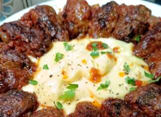 Ένα πιάτο με μακρόστενα σουτζουκάκια βουτηγμένα σε κόκκινη σάλτσα ντομάτας, δίπλα σε μια μεγάλη κουταλιά αφράτου πουρέ πατάτας.