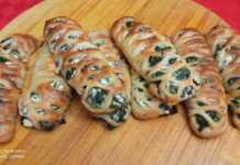 Εξι χρυσαφένια, φρεσκοψημένα σπανακοπιτάκια σε σχήμα πλεξούδας, τοποθετημένα σε λαδόκολλα, με ελαφρώς εμφανή τη γέμιση.