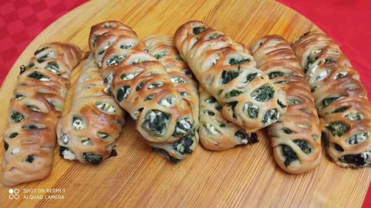 Εξι χρυσαφένια, φρεσκοψημένα σπανακοπιτάκια σε σχήμα πλεξούδας, τοποθετημένα σε λαδόκολλα, με ελαφρώς εμφανή τη γέμιση.