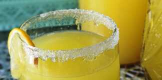 Μια κανάτα γεμάτη κιτρινωπή λεμονάδα με κομματάκια φρούτων και φυσαλίδες.