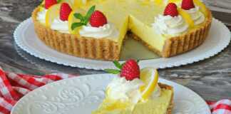 Ένα κομμάτι κρεμώδης τάρτα λεμονιού με μπισκοτένια βάση, κρεμώδη κίτρινη γέμιση, γαρνιρισμένη με φρέσκα βατόμουρα και δυόσμο, σερβιρισμένο σε ένα λευκό πιάτο.