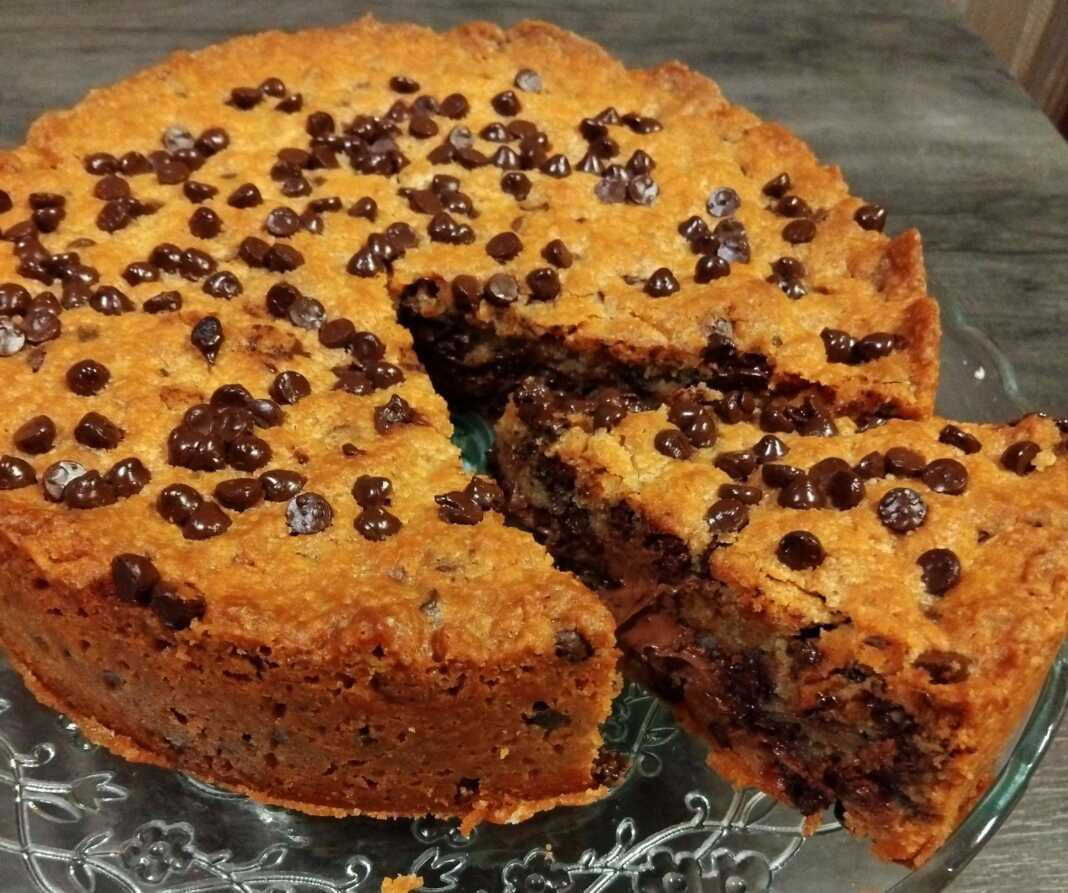 Μια στρογγυλή τάρτα μπισκότο γεμιστή με Nutella, πασπαλισμένη με σταγόνες σοκολάτας, σερβιρισμένη χλιαρή με μια μπάλα παγωτό.