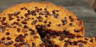 Μια στρογγυλή τάρτα μπισκότο γεμιστή με Nutella, πασπαλισμένη με σταγόνες σοκολάτας, σερβιρισμένη χλιαρή με μια μπάλα παγωτό.