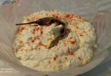 Ένα μπολ με λευκή, κρεμώδη σπιτική τυροκαυτερή, πασπαλισμένη με κόκκινη πάπρικα και γαρνιρισμένη με μια ολόκληρη πιπεριά τσίλι.