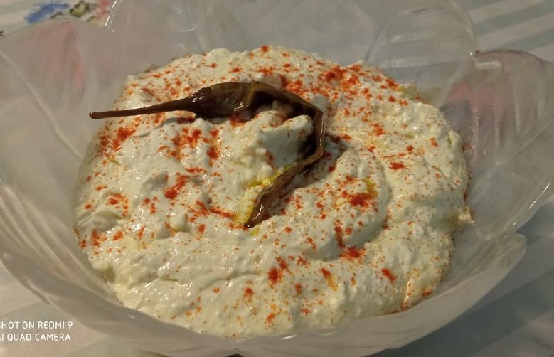 tirokafteri Ένα μπολ με λευκή, κρεμώδη σπιτική τυροκαυτερή, πασπαλισμένη με κόκκινη πάπρικα και γαρνιρισμένη με μια ολόκληρη πιπεριά τσίλι.