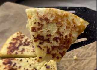 Λαχταριστή τηγανίτα με τυριά σε πιάτο, κομμένη σε κομμάτια, με λιωμένο βούτυρο στην επιφάνεια.