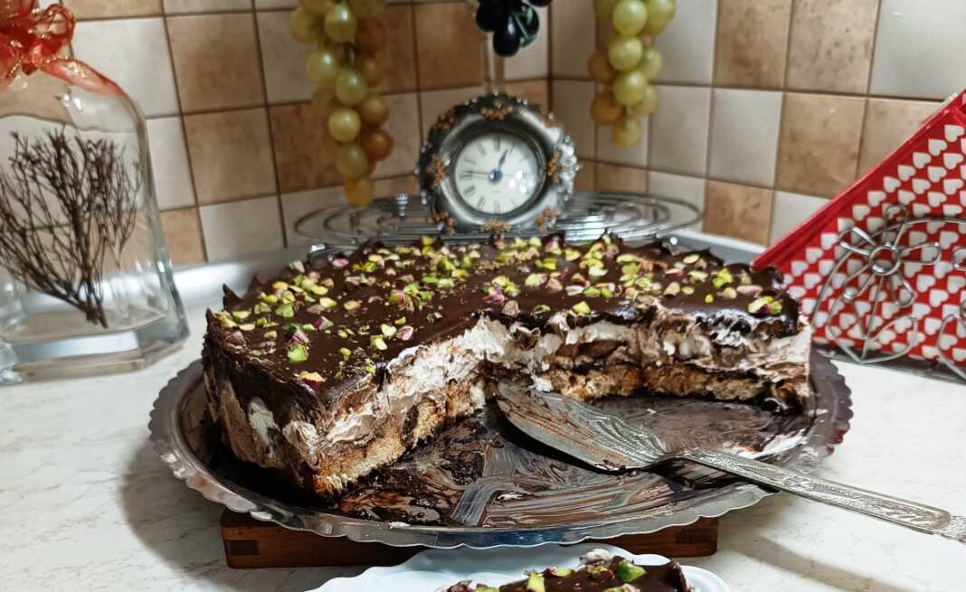 torta me tsoureki Μία τούρτα με βάση τσουρεκιού, στρώσεις λευκής και σοκολατένιας κρέμας, γλάσο σοκολάτας στην κορυφή και πασπαλισμένο με ψιλοκομμένο φιστίκι Αιγίνης.