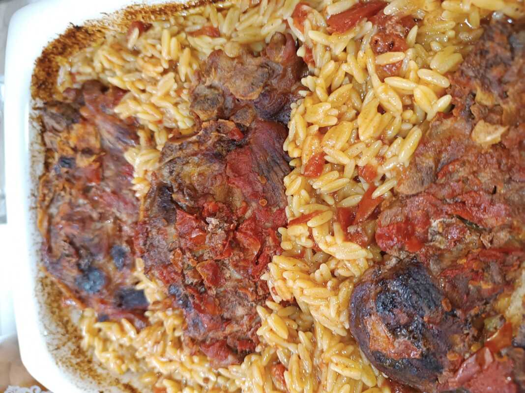 xoirines giouvetsi Ένα ταψί με λαχταριστό γιουβέτσι, με χρυσαφένιο κριθαράκι και κομμάτια χοιρινού κρέατος μέσα σε κόκκινη σάλτσα ντομάτας.