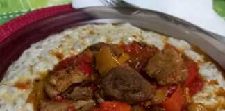 Ένα πιάτο με κομμάτια χοιρινού ανάμεσα σε χρωματιστές πιπεριές και δίπλα μια μεγάλη κουταλιά από έναν κρεμώδη, γκριζωπό πουρέ.