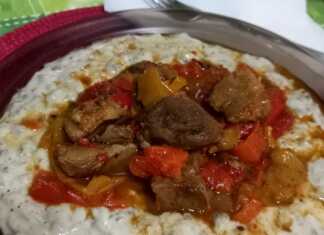 Ένα πιάτο με κομμάτια χοιρινού ανάμεσα σε χρωματιστές πιπεριές και δίπλα μια μεγάλη κουταλιά από έναν κρεμώδη, γκριζωπό πουρέ.