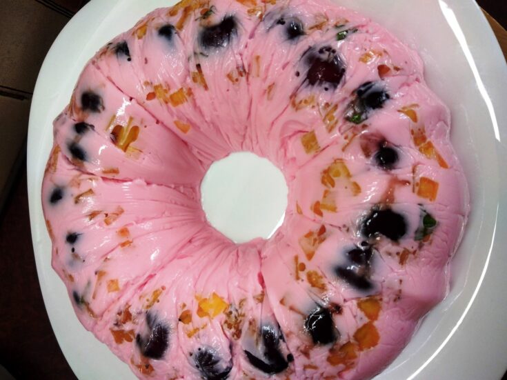 Ένα μπολ γεμάτο με ροζ γλυκό γιαούρτι και ζελέ, αναμεμειγμένο με κόκκινα κεράσια, κομματάκια νεκταρινιού, και πράσινα φυλλαράκια δυόσμου.