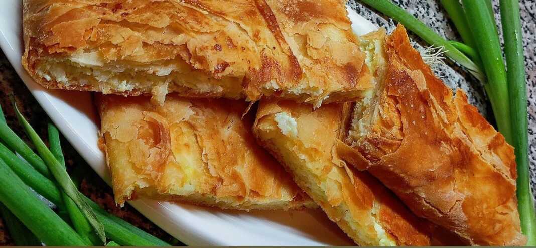 Κοντινό πλάνο σε ένα κομμάτι Ηπειρώτικης Ριζοτυρόπιτας, που αναδεικνύει τις στρώσεις του φύλλου και την πλούσια γέμιση ρυζιού και φέτας."