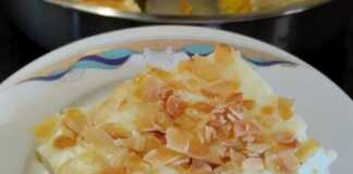 Κομμάτι Πορτοκαλόπιτας με ορατές τις στρώσεις παντεσπανιού, σιροπιού και κρέμας, πασπαλισμένο με αμύγδαλο.