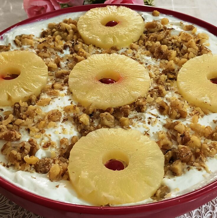 Ενα ταψί με δροσερό γλυκό γιαούρτι με κομματάκια ανανά, πασπαλισμένο με καρύδια, έτοιμο για σερβίρισμα.