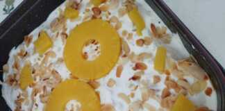 Ένα ολόκληρο Δροσερό Γλυκό με Ανανά, διακοσμημένο με ροδέλες ανανά και φιλέ αμυγδάλου, σε μία πιατέλα.