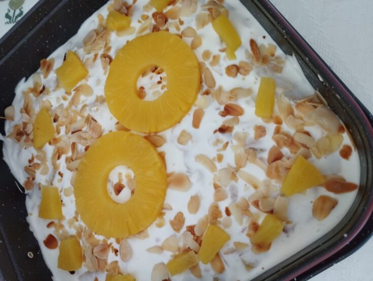 Ένα ολόκληρο Δροσερό Γλυκό με Ανανά, διακοσμημένο με ροδέλες ανανά και φιλέ αμυγδάλου, σε μία πιατέλα.