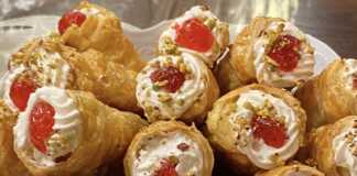 Πιάτο γεμάτο με γλυκά κορνεδάκια, γεμισμένα με λευκή κρέμα και γαρνιρισμένα με κόκκινο γλυκό του κουταλιού και ψιλοκομμένο φιστίκι, έτοιμα για σερβίρισμα.