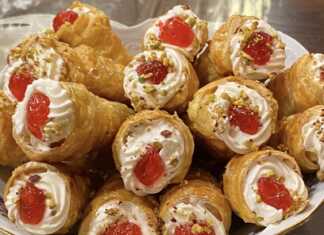 Πιάτο γεμάτο με γλυκά κορνεδάκια, γεμισμένα με λευκή κρέμα και γαρνιρισμένα με κόκκινο γλυκό του κουταλιού και ψιλοκομμένο φιστίκι, έτοιμα για σερβίρισμα.