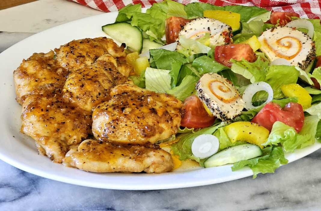 Πιάτο με σερβιρισμένο κοτόπουλο λεμονάτο και φρέσκια πράσινη σαλάτα.