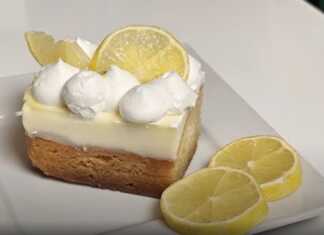 Κομμάτι από δροσερή λεμονόπιτα με πλούσια κρέμα βανίλιας και ξύσμα λεμονιού, πασπαλισμένο με σαντιγί, έτοιμο για σερβίρισμα.