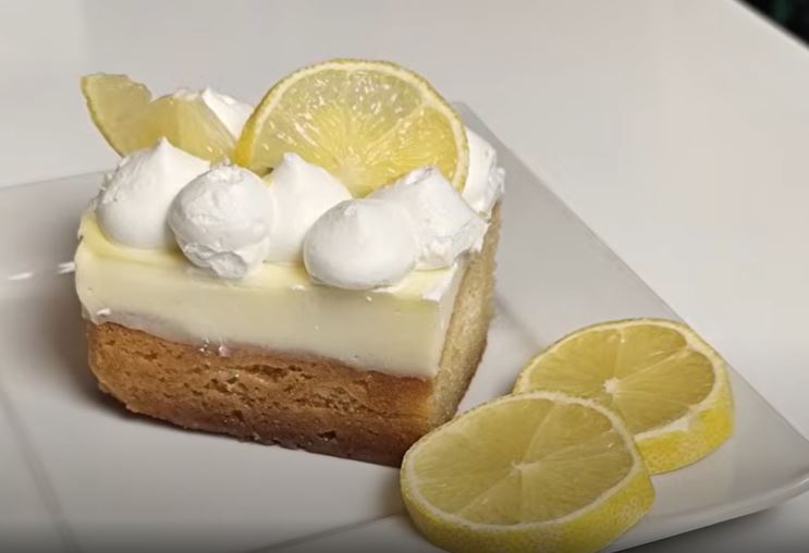 lemonopita me santigi Κομμάτι από δροσερή λεμονόπιτα με πλούσια κρέμα βανίλιας και ξύσμα λεμονιού, πασπαλισμένο με σαντιγί, έτοιμο για σερβίρισμα.