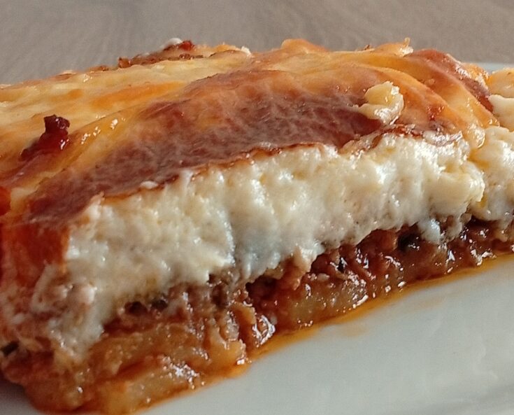 Κοντινό πλάνο σε μία μερίδα Μουσακά, που αναδεικνύει τις στρώσεις από πατάτες, μελιτζάνες, κιμά και την πλούσια μπεσαμέλ