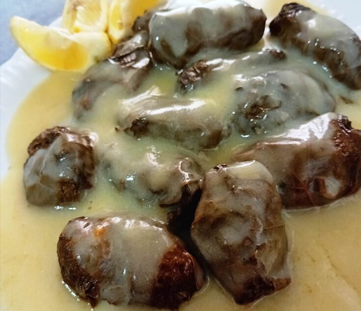 Ζεστά ντολμαδάκια με κιμά, περιχυμένα με χρυσαφένια σάλτσα αυγολέμονο, σε πιατέλα.