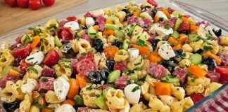 Πιάτο με πολύχρωμη σαλάτα τορτελίνια, γεμάτη λαχανικά, τυριά και σαλάμι, έτοιμη για σερβίρισμα σε καλοκαιρινό φόντο.