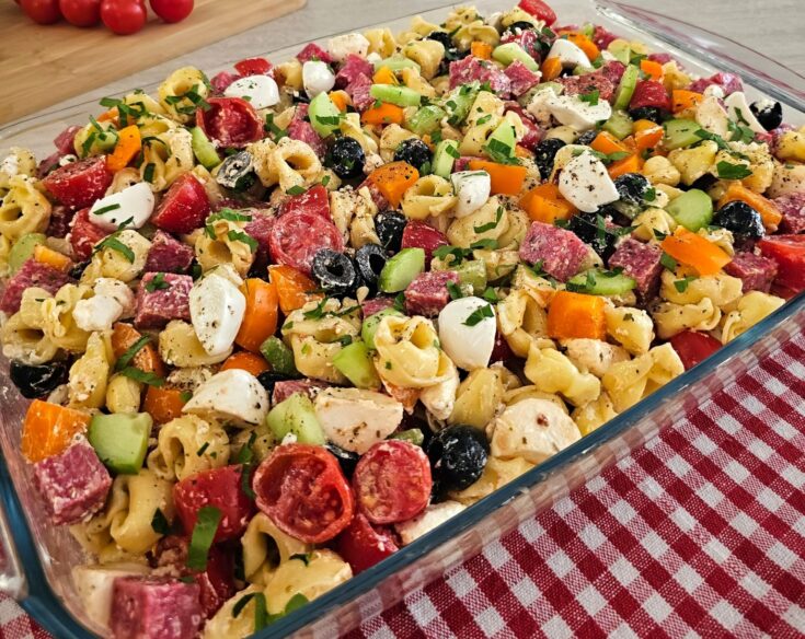 Πιάτο με πολύχρωμη σαλάτα τορτελίνια, γεμάτη λαχανικά, τυριά και σαλάμι, έτοιμη για σερβίρισμα σε καλοκαιρινό φόντο.