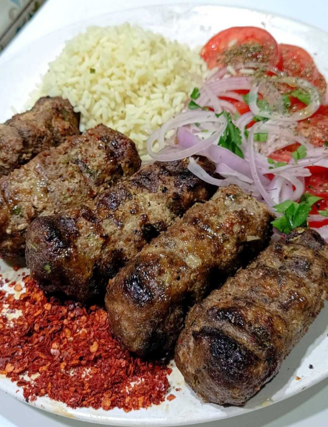 Πιάτο με σερβιρισμένα Σουτζουκάκια ψητά στα κάρβουνα, συνοδευόμενα από πιλάφι και ψιλοκομμένα λαχανικά.