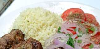 Πιάτο με σερβιρισμένα Σουτζουκάκια ψητά στα κάρβουνα, συνοδευόμενα από πιλάφι και ψιλοκομμένα λαχανικά.