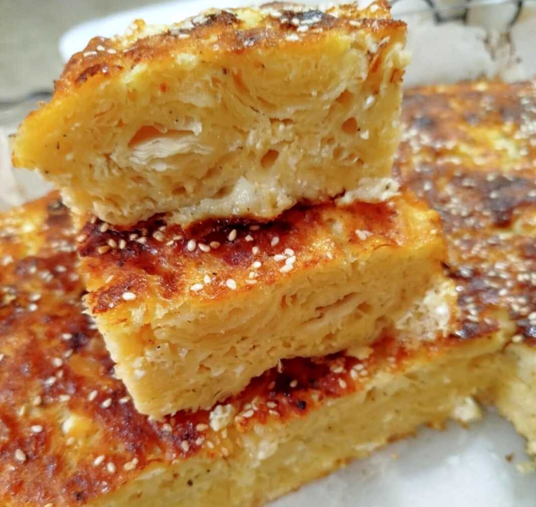 Πλούσια και αφράτη τυρόπιτα με φύλλα κρούστας, χρυσαφένια, κομμένη σε κομμάτια, πασπαλισμένη με σουσάμι, έτοιμη για σερβίρισμα.