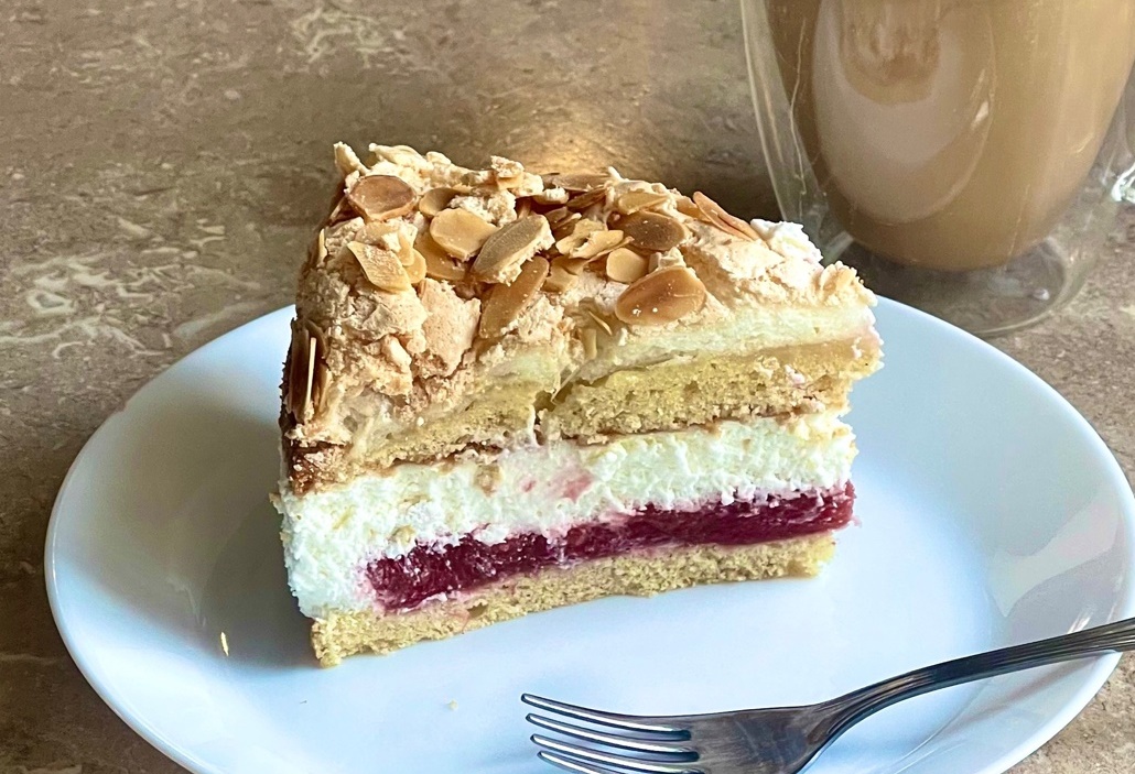 tourta paradeisenia Κομμάτι από Τούρτα Παραδεισένια, που αναδεικνύει τις διαφορετικές στρώσεις: αφράτο κέικ, τραγανή μαρέγκα, κόκκινη γέμιση φράουλας και λευκή κρέμα τυριού