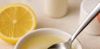 Κοντινό πλάνο ενός μικρού μπολ με λευκή βαζελίνη και φρεσκοστυμμένο χυμό λεμονιού, με ένα κουτάλι να ανακατεύει το μείγμα, σε ένα φόντο που υποδηλώνει περιποίηση δέρματος