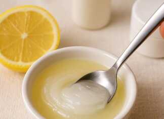 Κοντινό πλάνο ενός μικρού μπολ με λευκή βαζελίνη και φρεσκοστυμμένο χυμό λεμονιού, με ένα κουτάλι να ανακατεύει το μείγμα, σε ένα φόντο που υποδηλώνει περιποίηση δέρματος