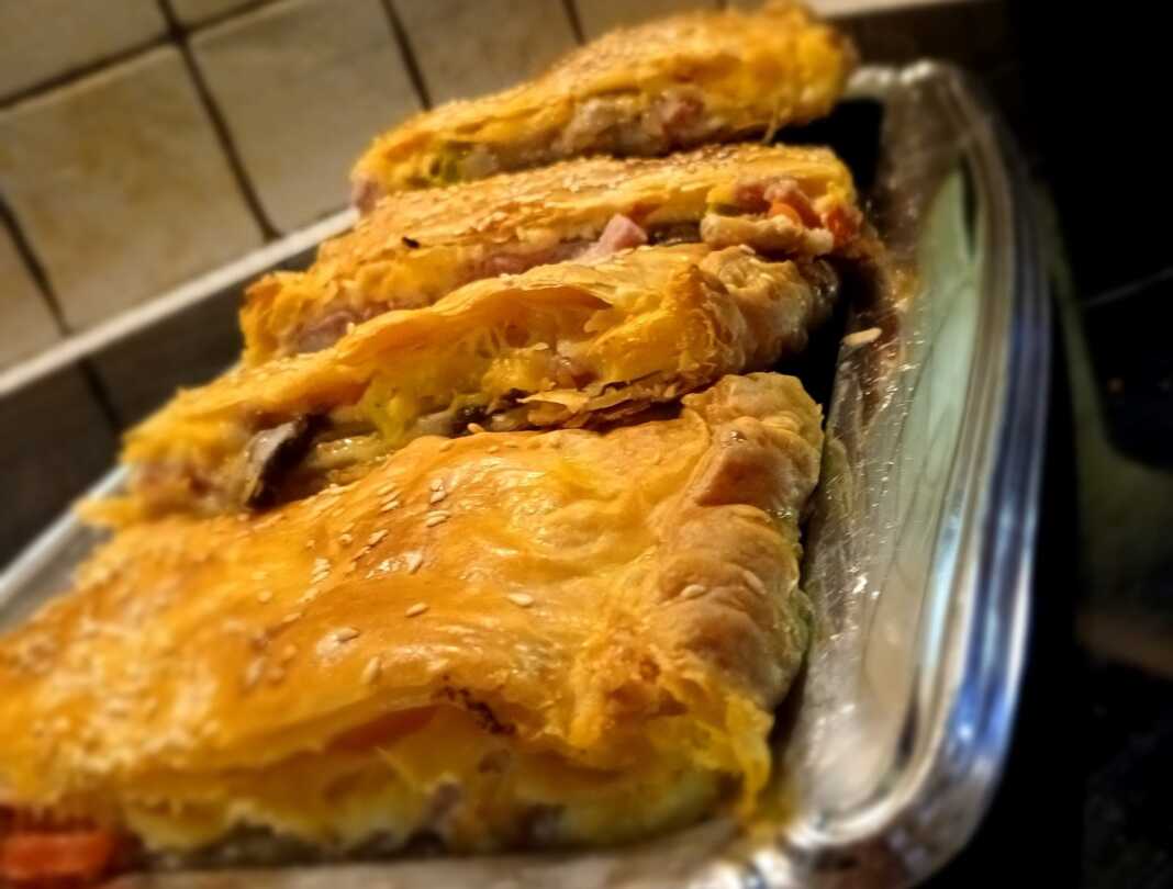 Κοντινό πλάνο σε κομμάτια από Ζαμπονοτυρόπιτα Σφολιάτας, που αναδεικνύει την πλούσια γέμιση με τυριά, ζαμπόν και λαχανικά