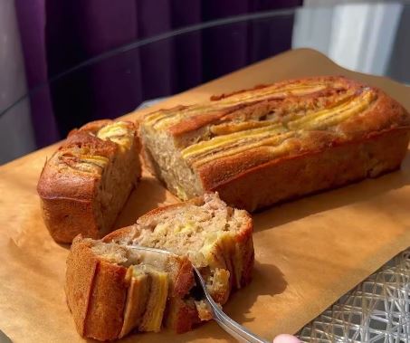 KEIKMPANANA Ένα ολόκληρο κέικ μπανάνας, φρεσκοψημένο, με μια μπανάνα κομμένη στη μέση από πάνω