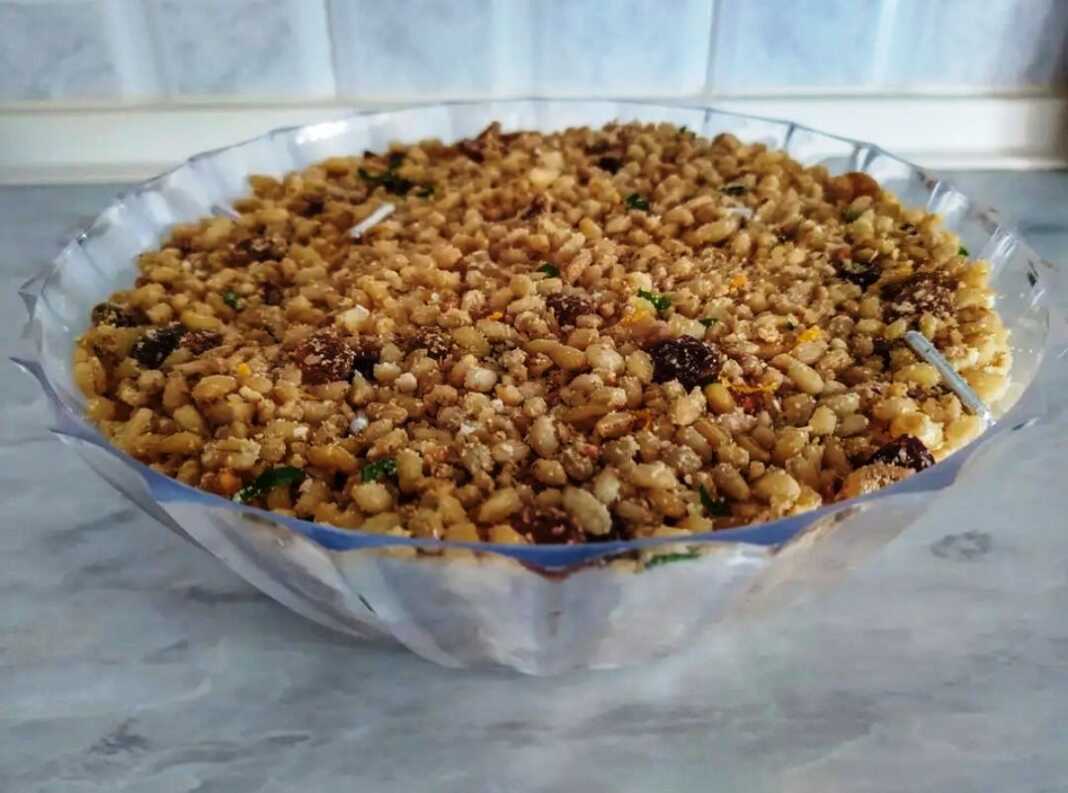 koliva Ένα μπολ με παραδοσιακά Κόλυβα, με την επιφάνεια καλυμμένη από άχνη ζάχαρη και διακοσμημένη με σταυρό από ασημένια ζαχαρωτά και σπόρους ροδιού