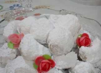 Ένα πιάτο γεμάτο με αφράτους Κουραμπιέδες ούζου, πασπαλισμένους με άφθονη ζάχαρη άχνη.