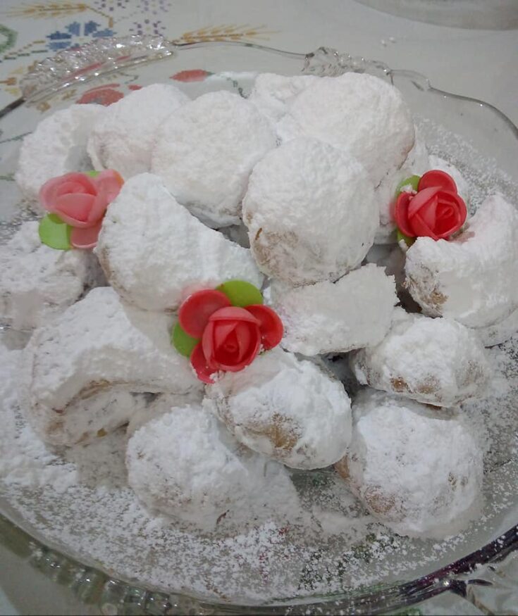 Ένα πιάτο γεμάτο με αφράτους Κουραμπιέδες ούζου, πασπαλισμένους με άφθονη ζάχαρη άχνη.