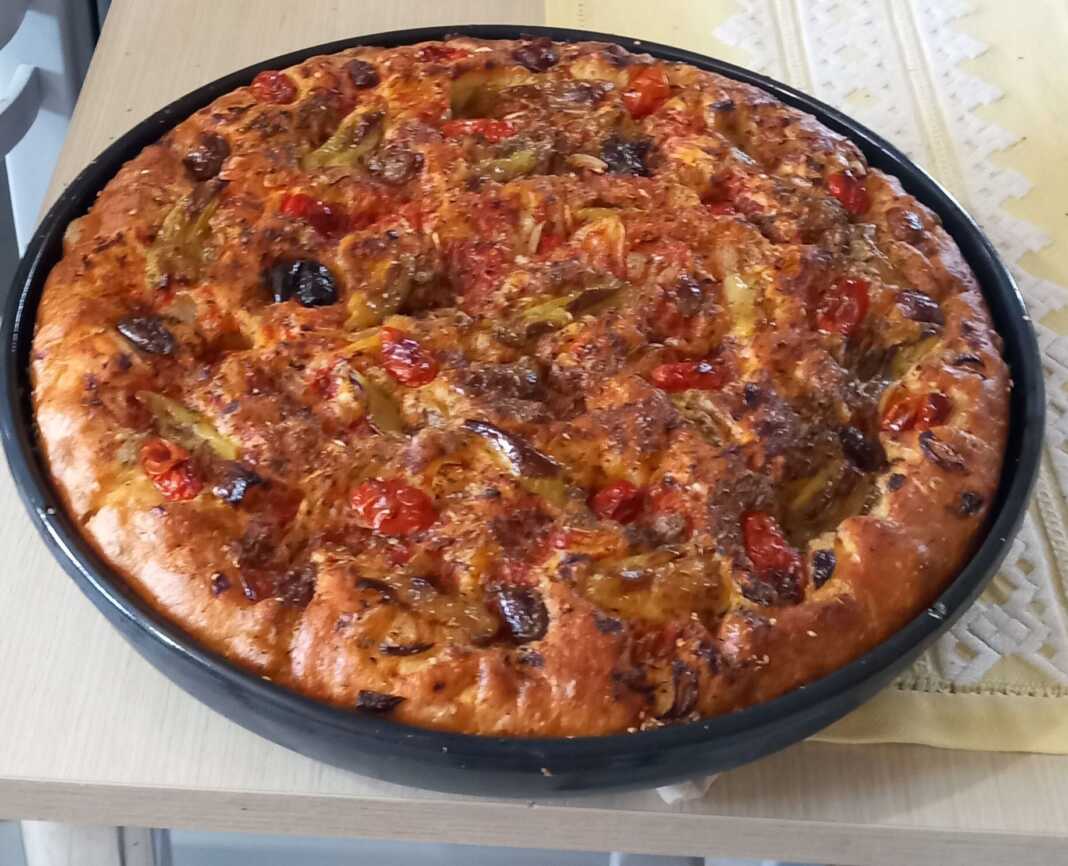 ladenia Ψημένη νηστίσιμη λαδένια σε ταψί, με πλούσια επικάλυψη από ντομάτα, κρεμμύδι και ελιές, έτοιμη για σερβίρισμα.